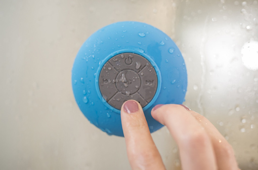 Démonstration de l'enceinte Bluetooth étanche fixée dans une douche avec main qui appuie sur les boutons